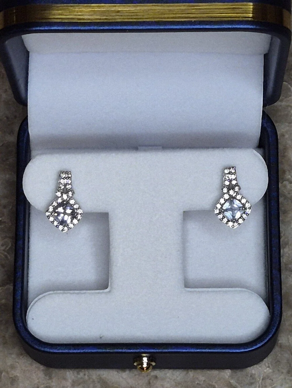 Brighton drop earrings feature a striking cushion-cut blue crystal center
